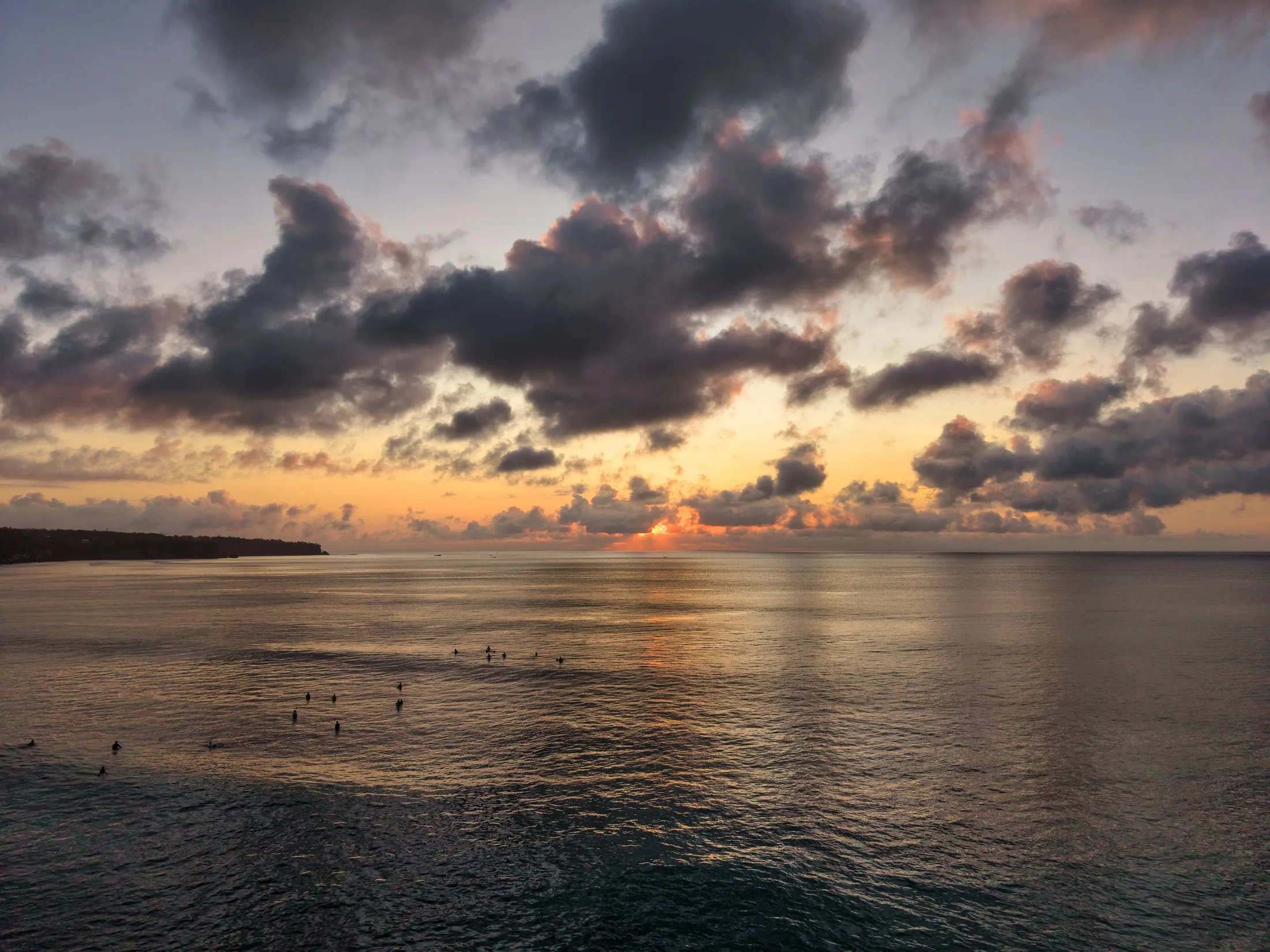 Paddleboarders on calm water beneath a tropical sunset